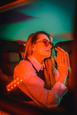 An attractive Spanish woman with sunglasses posing with red and green neon lights in a car