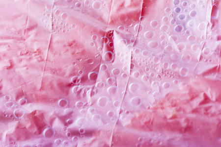A closeup of a wrinkled pink plastic cover with water droplets under itの写真素材