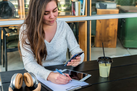 A young woman using her smartphone to rewrite a text on the paper in a cafeの写真素材