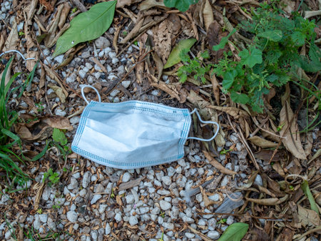 A selective focus shot of a used sanitary mask thrown on the ground near plantsの写真素材