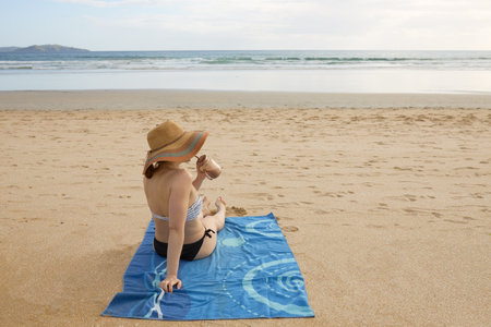A girl on the beach sitting on a towel and drinking natural nutritional juiceの写真素材