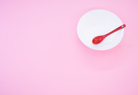 A high angle shot of a red spoon placed on a white bowl on a pink background shot on a studioの写真素材