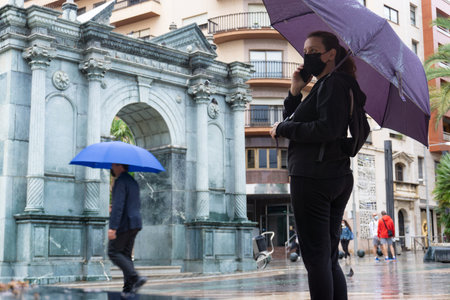 A caucasian female in a black protective mask standing outdoors with a purple umbrellaの写真素材