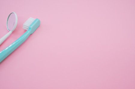 A blue toothbrush next to a dental mouth mirror on pastel pink surface for a copy spaceの写真素材