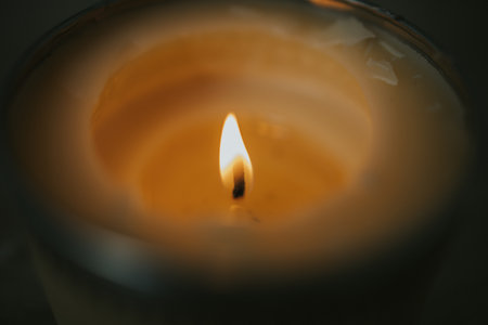 A selective focus shot of a candle flame burning a hole in the wax of a scented candleの写真素材
