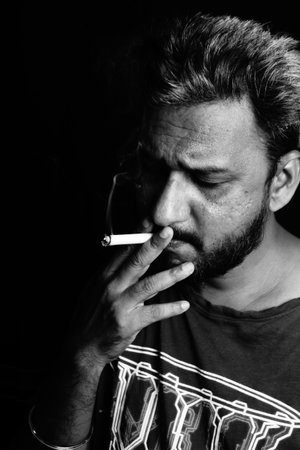 A black and white portrait of an attractive bearded Indian man smoking a cigaretteの写真素材