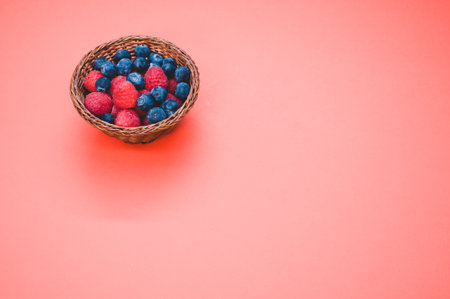 A high angle shot of fresh raspberries and blueberries in a basket isolated on red backgroundの写真素材