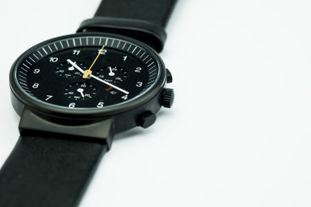 A closeup of a simple black hand watch laid flat on a plain white surfaceの写真素材