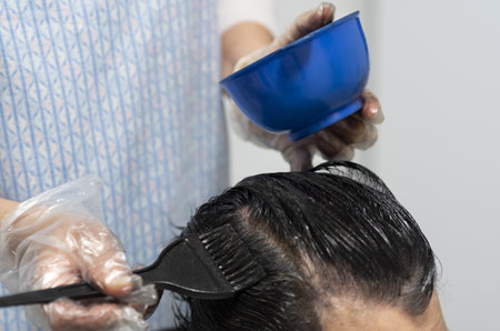 A hairdresser with single-use plastic gloves dying a woman's hair roots with a hairbrushの写真素材