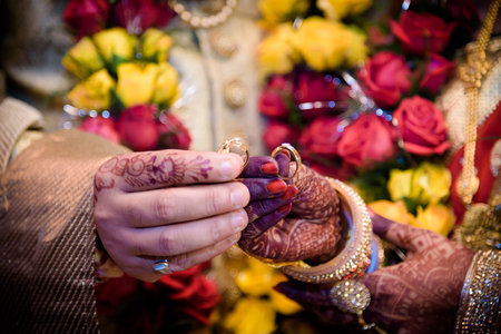 A shallow focus of an Indian couple with Mehndi on their hands holding wedding ringsの写真素材