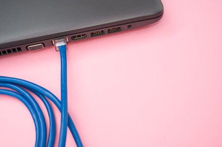 A closeup of a LAN cable connected to a laptop isolated on a pink backgroundの写真素材