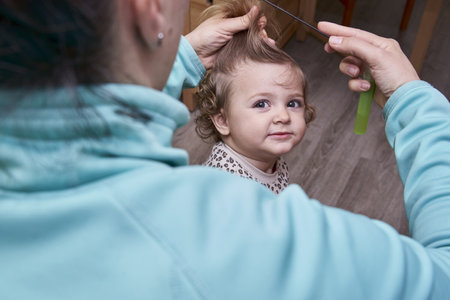 A cute view of the mother doing the hair of the kid, trying to separate hair with the combの写真素材