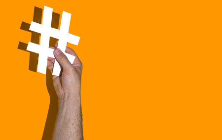 A man's hand holding a white hash on an orange background - social media day conceptの写真素材