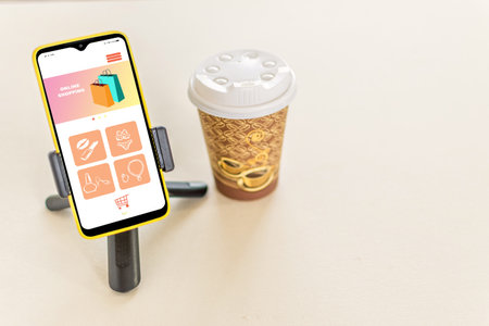 A takeaway cup of coffee and smart phone with a shopping app - online shopping conceptの写真素材