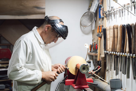 A woodworker with a safety mask on shaping a piece of wood on the latheの写真素材