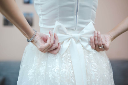 A shallow focus of the bride fixing the bow on her wedding dress with a blurry backgrouの写真素材
