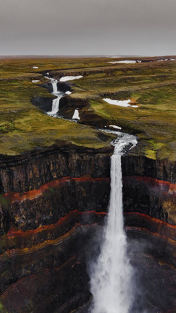 A vertical aerial shot of a waterfall in Iceland with textured rocks and water stream