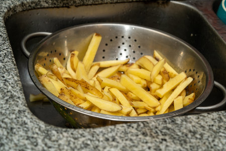 A closeup shot of fresh raw sliced french fries in a deep metal utensilの写真素材