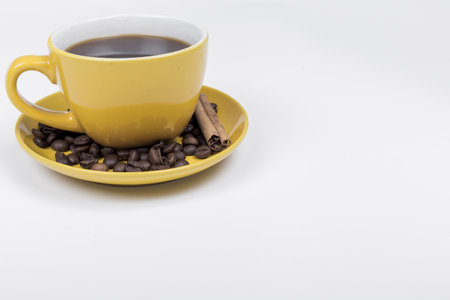 coffee composition, yellow ceramic cup full of black coffee, on the coffee saucer there are coffee beans and a cinnamon stick, the background is whiteの写真素材