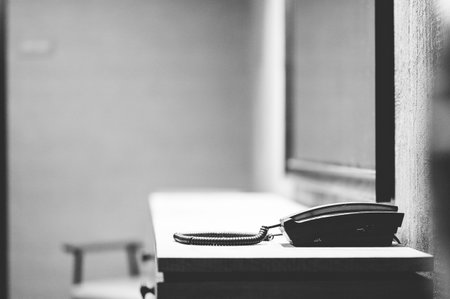 A grayscale shot of a jail telephone on a table next to the windowの写真素材