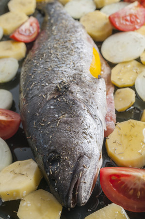 A vertical shot of sea bass with potatoes onions and tomatoes