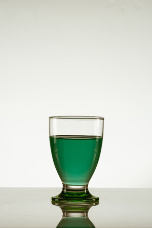 A vertical shot of a glass of green drink isolated on a reflective surfaceの写真素材