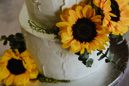 A closeup of a two-floor wedding cake decorated with sunflowers on a tray on the tableの写真素材
