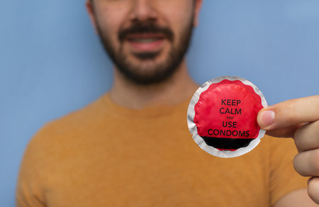 A man holding a condom with 'keep calm and use condoms' to prevent sexually transmitted diseases