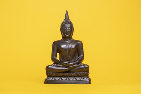 Small bronze Thai buddha statue against a yellow seamless background in meditative postureの写真素材