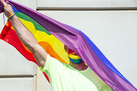 A man with a rainbow pride flag and a colorful maskの写真素材