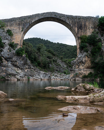 A beautiful view of an arch of the ancient bridge surrounded by trees on a gloomy dayの写真素材