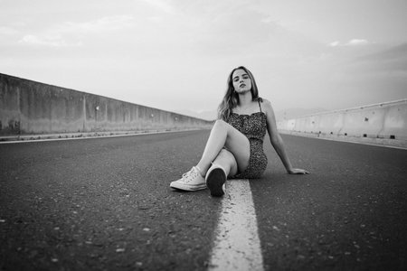 A grayscale shot of a young Caucasian female posing outdoors sitting on the streetの写真素材