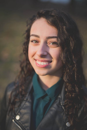 A beautiful curly Bosnian Caucasian woman in a black leather jacket posing outside