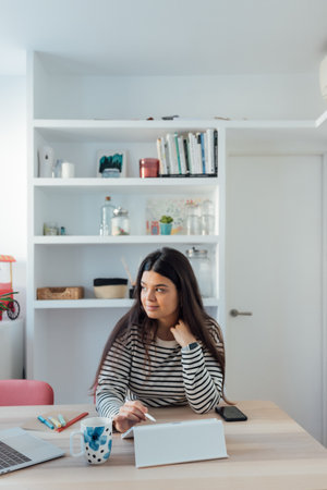A smiling young Spanish lady sitting at the desk and using a tabletの写真素材