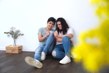 young  couple happily look at the result of a pregnancy test. they are sitting on the floor of their home. indoor natural light. fertility conceptの写真素材