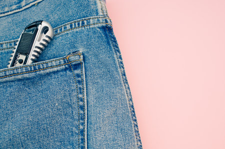 A closeup shot of a pocket knife in the jeans pocket on a pink backgroundの写真素材