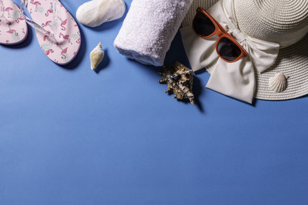 A top view of sunglasses, a straw hat, sandals, a towel and sea shells on a blue backgroundの写真素材