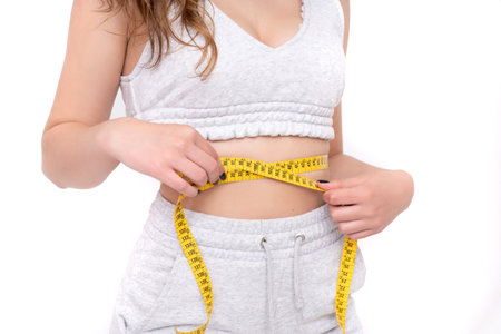 A closeup of a slim woman's measuring her thin waist on a white backgroundの写真素材