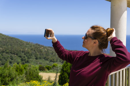 A middle-aged female taking a selfie at an observation deck with a view of the sea