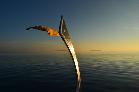 A closeup of a ship's wooden prow taken off and used as a flag pole on a tropical background during sunsetの写真素材