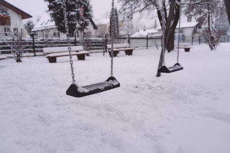 A closeup of swings in a playground covered in the snow in winterの写真素材