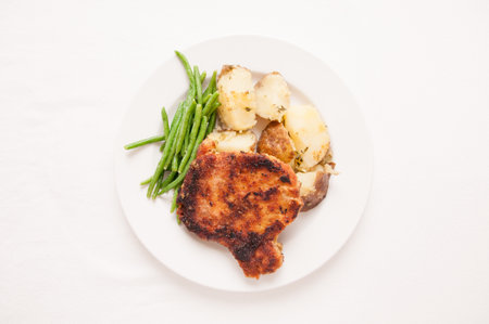 pan searched pork chop breaded with herbs and spices with herb encrusted potato and haricote vertの写真素材