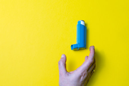 A hand holding an asthma inhaler on  yellow backgroundの写真素材