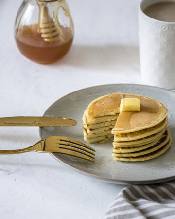 A picture of a stack of pancakes been cut, showing the layers. we can see milk coffee and honey in the background.の写真素材