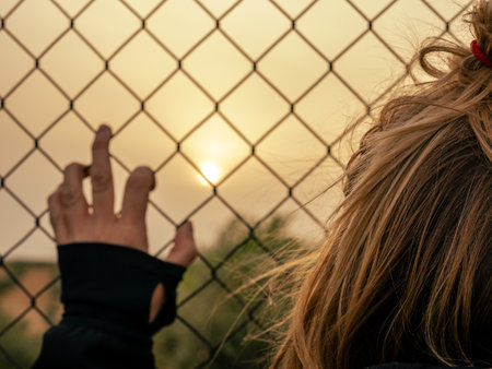Blond woman leaning on a fence at sunsetの写真素材