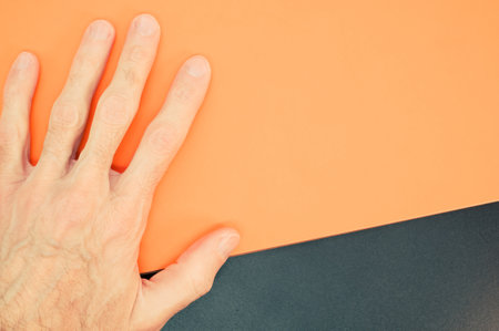 A closeup shot of a hand and a black mat texture on an orange backgroundの写真素材