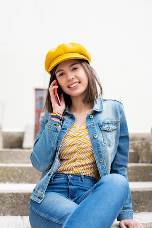 A young female in a yellow cap and denim jacket talking on the phoneの写真素材