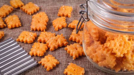 A closeup of bite size cheese crackers in a jar and on a wooden table with a rolling pin and...
