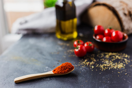 A spoon with spices, cherry tomatoes and a bottle of olive oil on a dark table