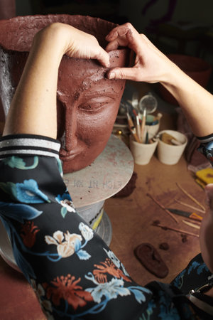 A closeup shot of hands sculpting a clay vase with a faceの写真素材